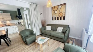 A modern living room with a sofa, two armchairs, a coffee table, and a dining area with a table and chairs. - Charming Renovated Apartment, Central Jullouville, 1 Bed, 4 Guests, Parking, 100m from Beach (Jullouville)