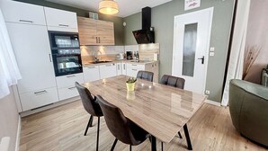 A modern kitchen with white cabinets, a wooden dining table, and a green sofa. - Charming Renovated Apartment, Central Jullouville, 1 Bed, 4 Guests, Parking, 100m from Beach (Jullouville)