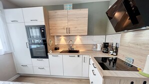 A modern kitchen with white cabinetry, a built-in oven, a sink, and a coffee maker. - Charming Renovated Apartment, Central Jullouville, 1 Bed, 4 Guests, Parking, 100m from Beach (Jullouville)