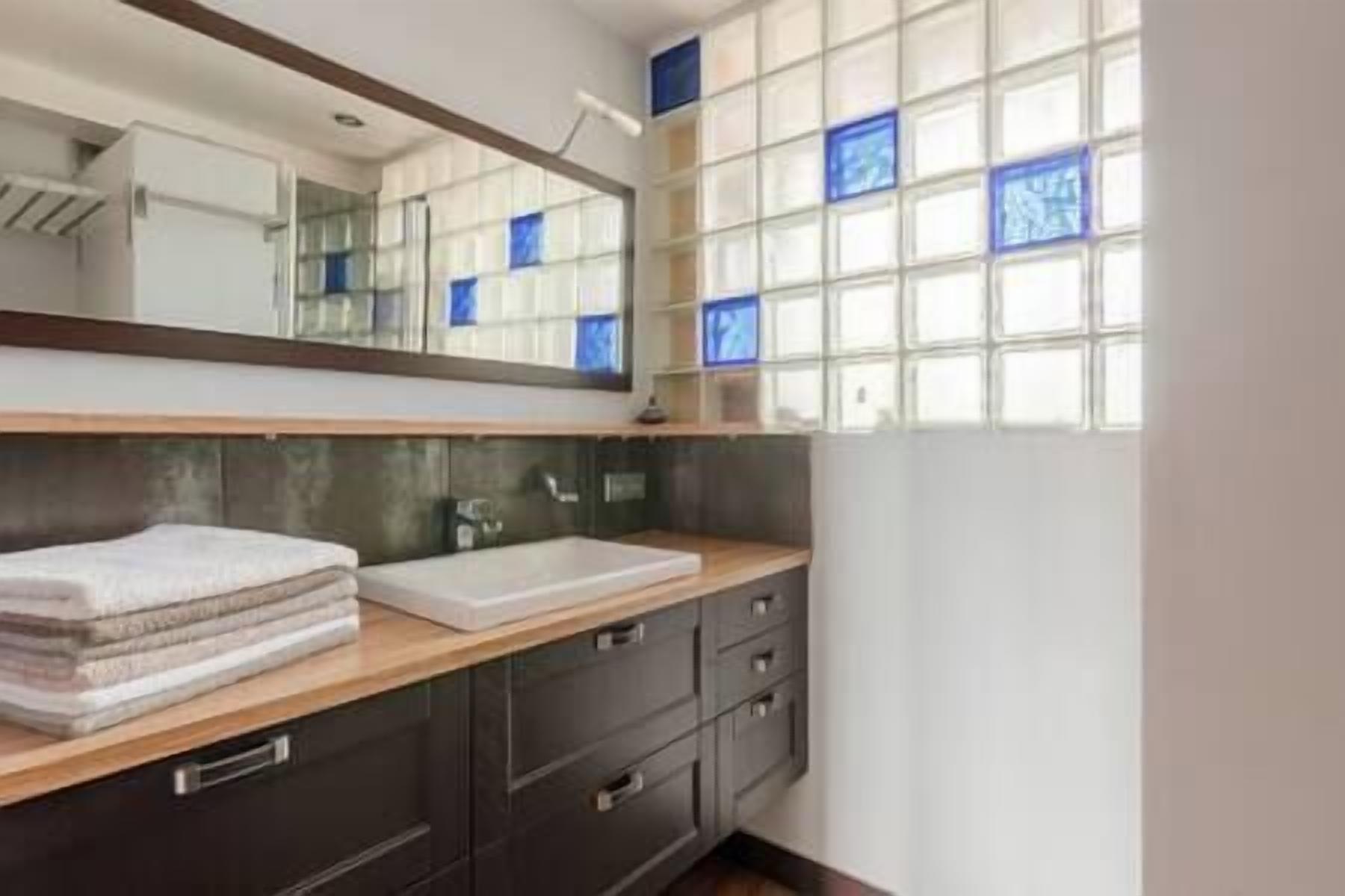 Un bany amb un mirall gran, un lavabo i una finestra amb vidres blaus.
