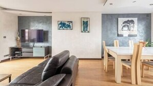 Un salon moderne comprenant un canapé, un téléviseur et un coin repas avec des chaises et une table.