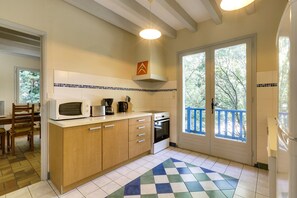 A kitchen with a microwave, stove, and cabinets, a dining area with a chair, and a view through a door to the outside.