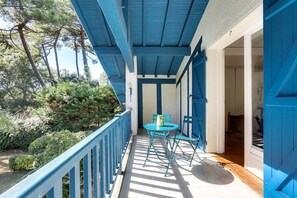 A balcony with blue railings, a table with chairs, and a view of a garden with trees.