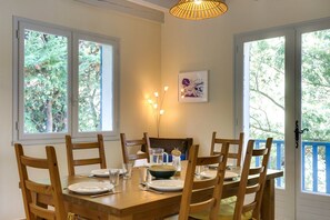 A dining table set for four with chairs, a hanging light fixture, and a window with a view of trees. - Hossegor Lake, 10 pers Villa (SEIGNOSSE)