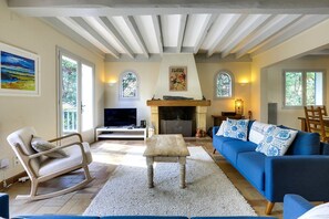 A living room with a fireplace, a sofa, a television, and a rocking chair. - Hossegor Lake, 10 pers Villa (SEIGNOSSE)
