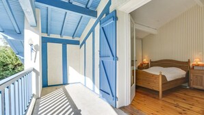 A bedroom with a wooden bed, bedside tables with lamps, and a balcony with blue shutters. - Hossegor Lake, 10 pers Villa (SEIGNOSSE)