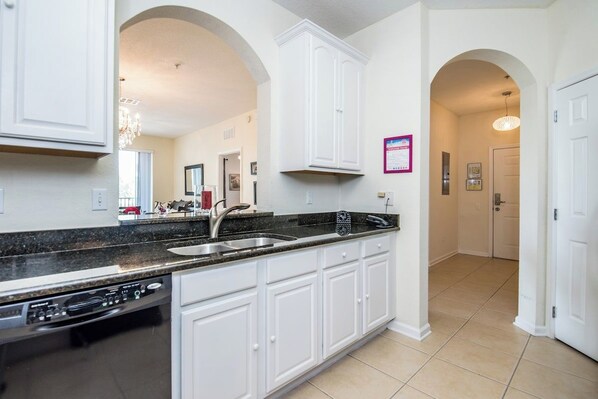 A kitchen with white cabinets, a black countertop, and a dishwasher.