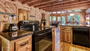 Cocina rústica de cabaña con paredes de madera, una isla central, una estufa, un lavavajillas y un letrero que dice "IN SWEET CABIN".