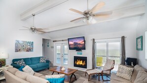 A spacious living room with a fireplace, a ceiling fan, and a large TV mounted on the wall. - Pelicans Place LCV23 has great views from 2 decks, and is close to white sandy b (Port Aransas)