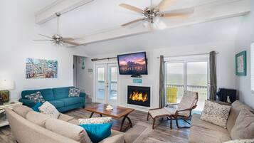 A spacious living room with a fireplace, a ceiling fan, and a large TV mounted on the wall.