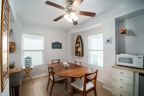 A dining area with a wooden table, chairs, a ceiling fan, and a microwave on a counter.