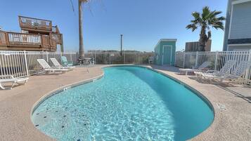 A clear swimming pool with lounge chairs and a fenced deck area.