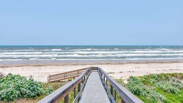 A wooden boardwalk leading to a beach with waves in the background.