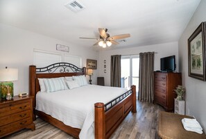 A bedroom with a wooden bed, a ceiling fan, a television, and a balcony with curtains.