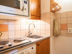 Compact kitchen with a microwave, sink, stove, and cabinet.