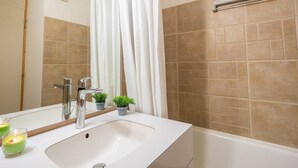 Un baño con un lavabo blanco, un espejo, un perchero para toallas y una zona de ducha con azulejos color beige.