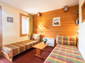 Cozy room with two single beds, a wooden table, and a chair, featuring a window with a curtain.