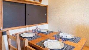 Comedor con una mesa de madera dispuesta para cuatro personas, rodeada de sillas. Encima de la mesa, hay un estante de madera con objetos decorativos.