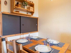 A dining area with a table set for four, featuring a geometric-patterned placemat and a vase with flowers on a nearby shelf.