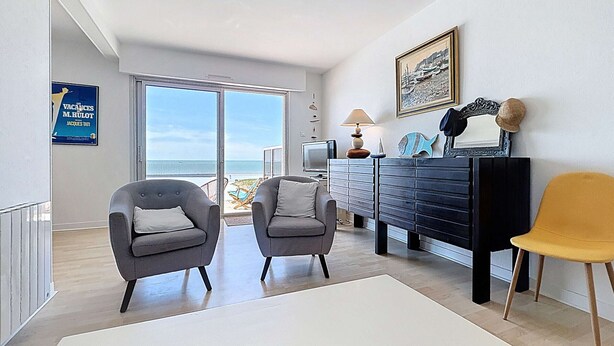 A modern living room with two grey armchairs, a white coffee table, a black dresser, and a yellow chair. A large window offers a view of the beach. - Seaside apartment with terrace and parking (Jullouville)