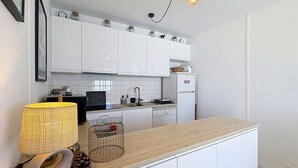 A modern kitchen with white cabinets, a wooden countertop, a built-in stove, and a small refrigerator. - Seaside apartment with terrace and parking (Jullouville)