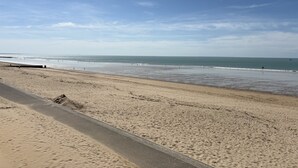 A beach with a paved walkway, calm sea, and clear sky. - Seaside apartment with terrace and parking (Jullouville)