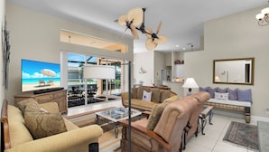A spacious living room with a large flat-screen TV, comfortable seating, a ceiling fan, and a view of the outdoors.