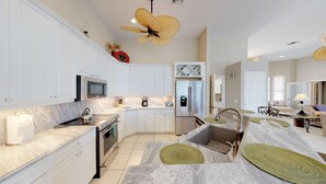 A modern kitchen with white cabinets, a stainless steel refrigerator, a microwave, and a large ceiling fan.