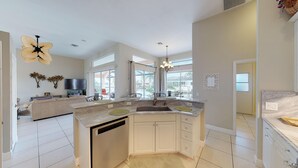 A modern kitchen with a large island, a dining area, and a living room with a TV.