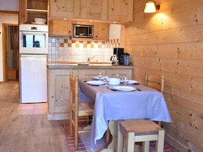Uma cozinha aconchegante com armários de madeira, micro-ondas, fogão e uma área de jantar para quatro pessoas, com a mesa posta para refeição.