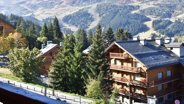 A mountain lodge with multiple balconies, surrounded by dense forest and a view of distant hills.
