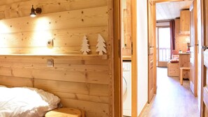 A wooden cabin interior with a bed, a small stool, and a wooden shelf with Christmas tree decorations.