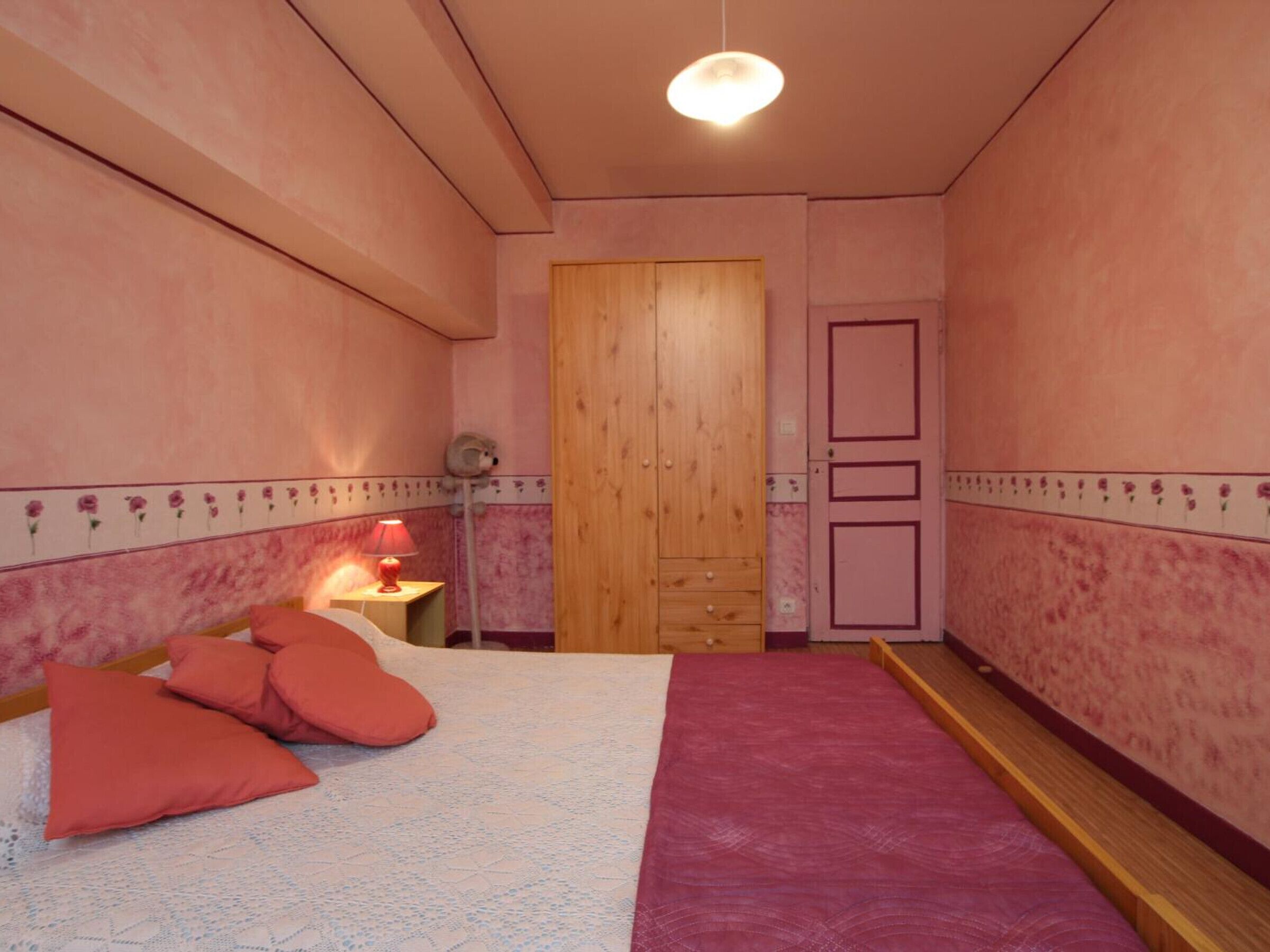 Une chambre à coucher avec un lit, des oreillers, une table de chevet avec une lampe, une armoire en bois et une porte.