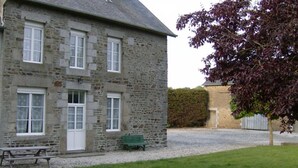 Un bâtiment en pierre doté de nombreuses fenêtres, un banc et un arbre au premier plan.