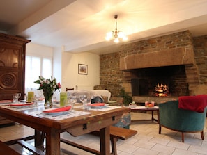 A cozy living room with a stone fireplace, wooden furniture, and a dining area set for a meal. - Countryside house in Mortain - 4 bedrooms, pets allowed, fireplace (Mortain)