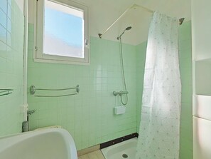 A bathroom with a bathtub, a shower with a handheld showerhead, a window, and a patterned shower curtain.