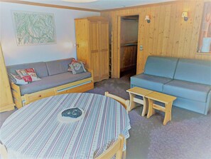 Una habitación acogedora con suelo de madera, dos sofás, una mesita redonda y un armario de madera.