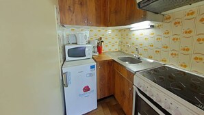 A compact kitchen with wooden cabinets, a microwave, a small refrigerator, a sink, and a stove.