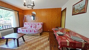 A cozy room with a wooden floor, a sofa, a dining table set for two, and a chandelier.