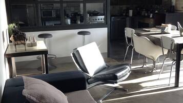 Ein modernes Wohnzimmer mit einer Couch, einem Essbereich mit Tisch und Stühlen sowie einer Küche im Hintergrund.
