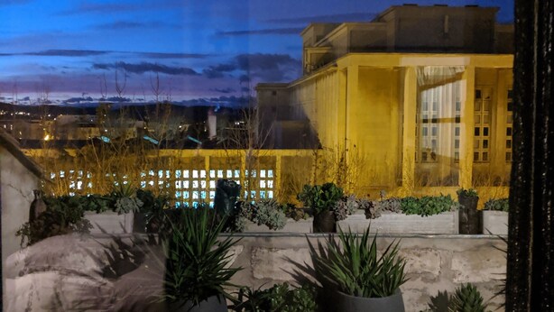 A rooftop terrace with potted plants, a dining table, and a view of a cityscape at dusk. - Stylish loft in the centre of Narbonne. View of the cathedral. Quality services (Narbonne)