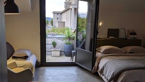 A modern bedroom with a bed, a chair, a desk, and a large window. - Stylish loft in the centre of Narbonne. View of the cathedral. Quality services (Narbonne)