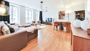A modern living room with a sofa, coffee table, and dining area. There is a TV, a fan, and a bookshelf in the background. - Tussaud spa 75m2 city center up to 4 (Colmar)
