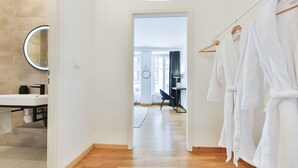 A hotel bathroom with a wooden floor, a sink, a mirror, and a rack with white robes. - Tussaud spa 75m2 city center up to 4 (Colmar)