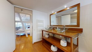 Ein modernes Badezimmer mit einem Waschbecken aus Glas, einer Holzkommode und einem großen Spiegel.