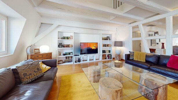 Ein geräumiges Wohnzimmer mit großem Flachbildfernseher, Ledersofas, Holzregalen und einem Glastisch.