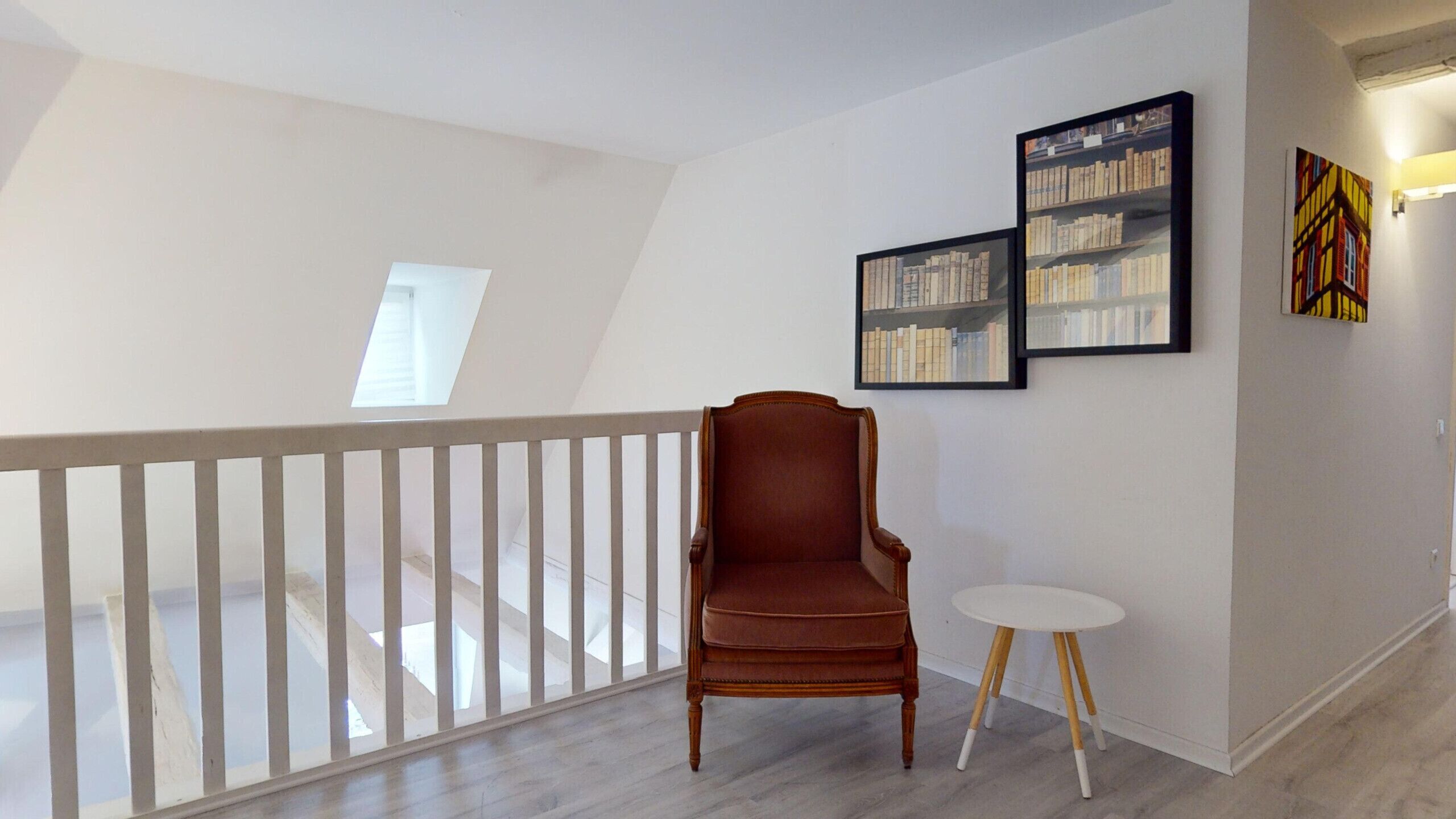 A room with a wooden chair, a small white table, and two framed pictures on the wall.