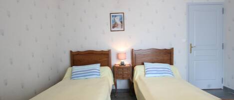 A room with two single beds, a nightstand with a lamp, a framed picture on the wall, and a white door.