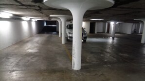 Ett underjordiskt parkeringsgarage med betongpelare, en vit bil parkerad en bit bort och en gul linje som markerar parkeringsplatserna.