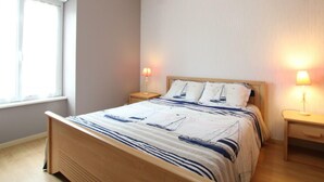 A bedroom with a bed, two bedside tables, a window, and a wall-mounted lamp.